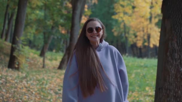 Vue de face de Belle jeune femme souriante et heureuse portant un sweat à capuche rose marchant dans le parc d'automne. Saison et concept de personnes. Nature, ralenti. — Video