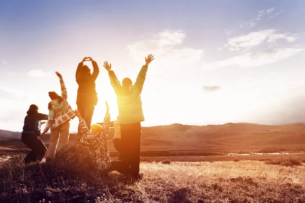 Turistas felizes com braços levantados contra o pôr do sol — Fotografia de Stock