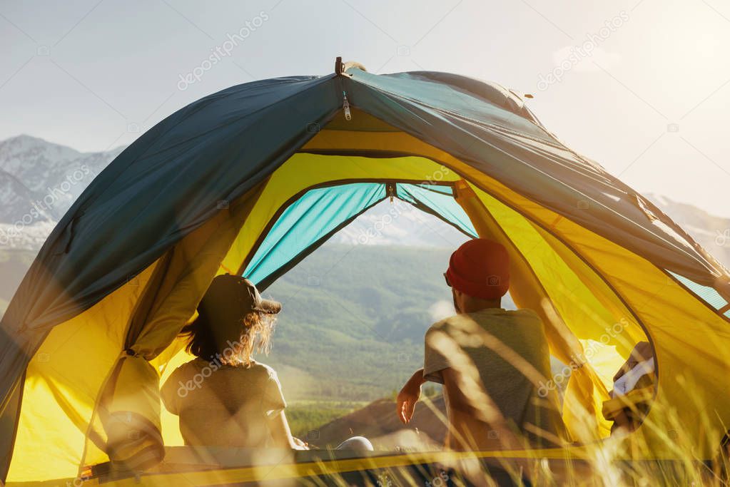 Couple rest in tent against mountains sunset