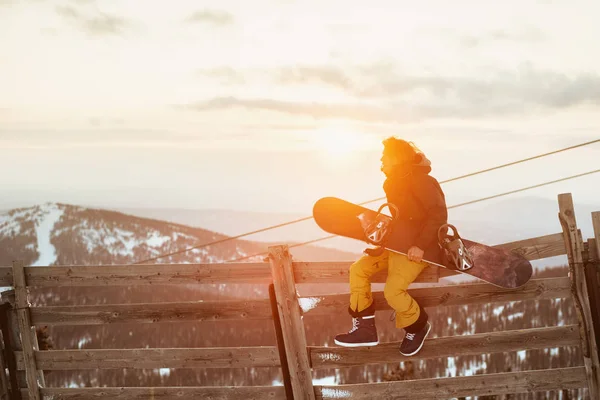 Snowboardzista siedzi na płocie z snowboard — Zdjęcie stockowe