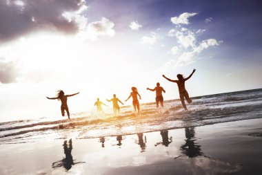 Grup mutlu halkların siluetleri günbatımı plaj çalıştırmak