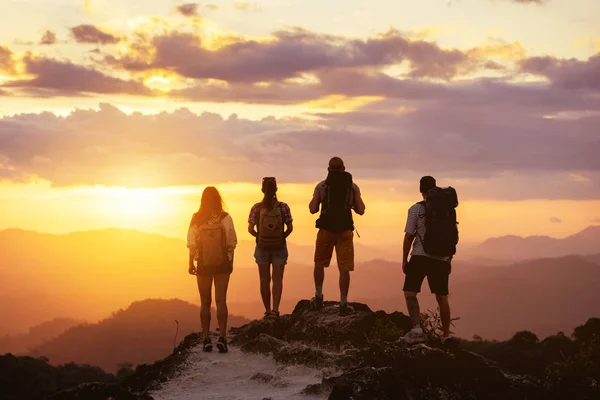 Quatro silhuetas de peopes no topo da montanha olha para o pôr do sol — Fotografia de Stock