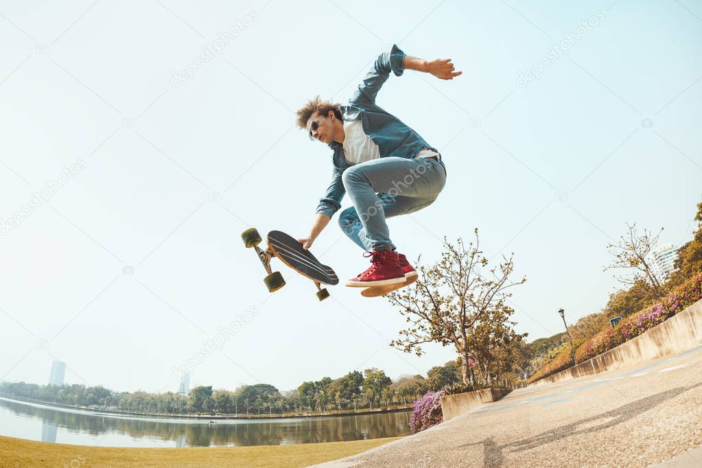 Hipster jumps with skateboard in park