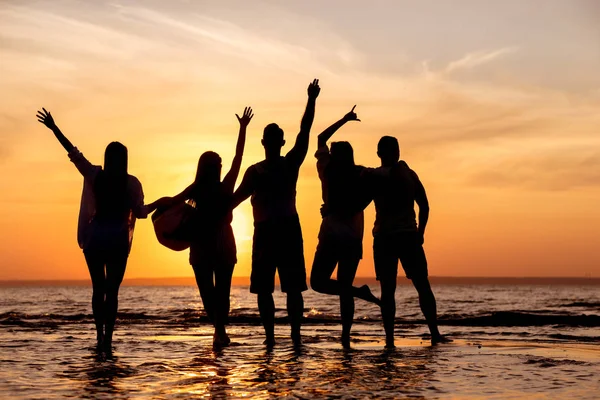 Felices siluetas de amigos en la playa del atardecer —  Fotos de Stock