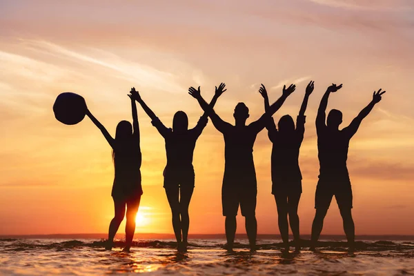 Amigos felizes com as mãos levantadas na praia do pôr do sol — Fotografia de Stock