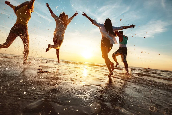 Amici felici alla festa in spiaggia corre verso l'acqua del tramonto — Foto Stock