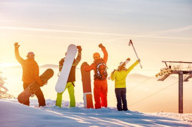 Gün batımı dağ tepesinde mutlu kayakçılar ve snowboardcular