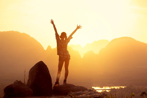 Happy slim girl stands with raised arms against sunrise or sunset, sea and islands. Phang Nga province, Thailand