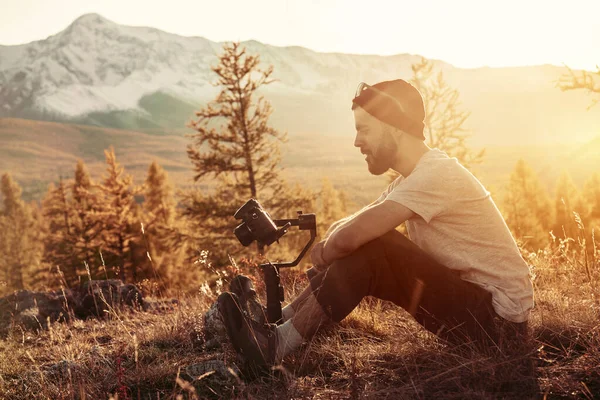 Homme assis avec cardan et caméra contre les montagnes — Photo