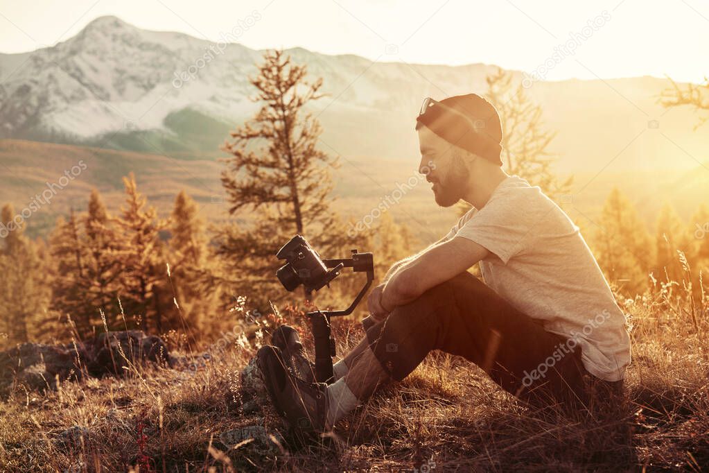 Man sits with gimbal and camera against mountains