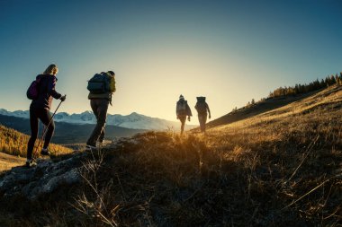 Bir grup yürüyüşçü gün batımında dağlarda yürür.