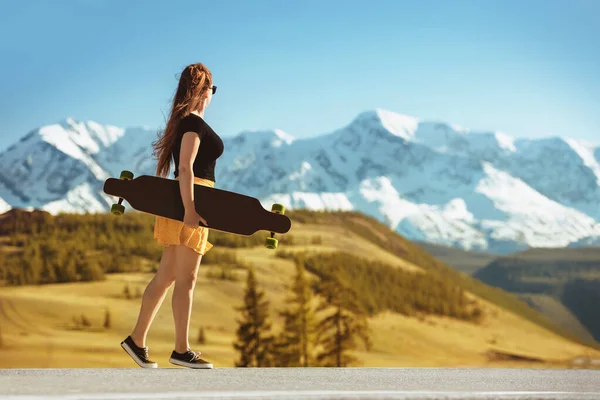 Young girl with longboard on mountain road — Stok fotoğraf