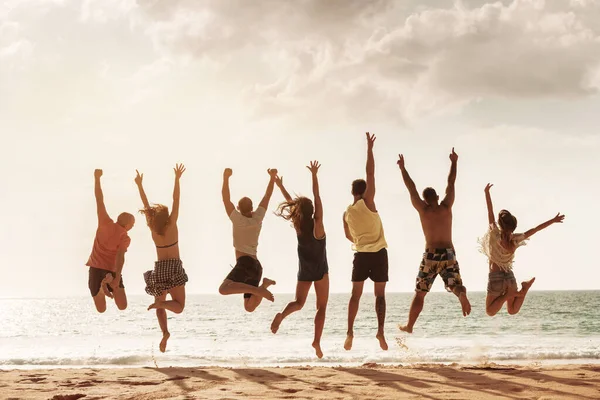 Amigos felizes salta juntos na praia do mar — Fotografia de Stock