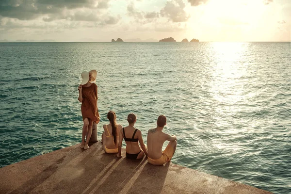 Mladí lidé sedí při západu slunce na mořském molu — Stock fotografie