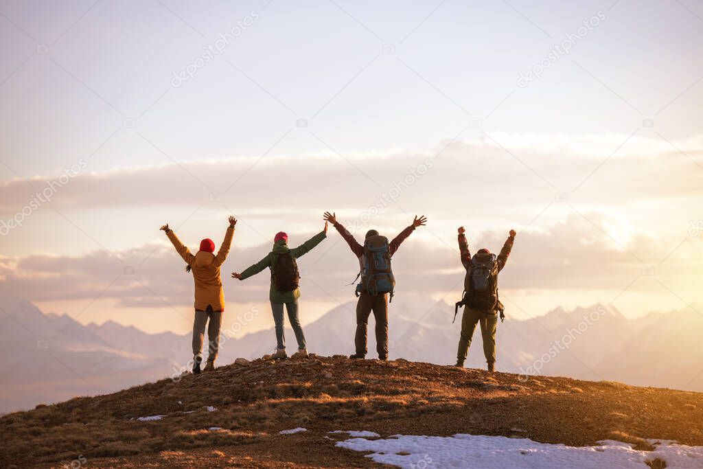 Four tourists stands at mountain top at sunset