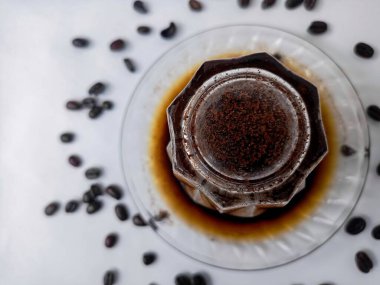 Kahve çekirdekleri etrafa saçılmış, kahve fincanında servis edilen taze demlenmiş kahve, yaşam tarzı ve kafe kültürünü temsil ediyor..