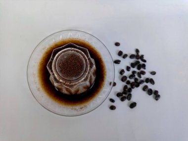 Kahve çekirdekleri etrafa saçılmış, kahve fincanında servis edilen taze demlenmiş kahve, yaşam tarzı ve kafe kültürünü temsil ediyor..