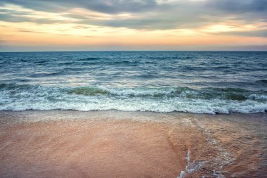 Gün batımının arka planında fırtınalı okyanus ve kumlu kıyı