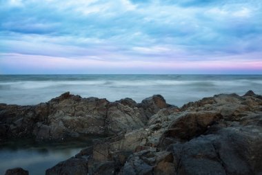 Gün batımının arka planında fırtınalı okyanus ve taşlı kıyı