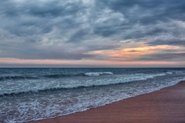 Gün batımının arka planında fırtınalı okyanus ve kumlu kıyı