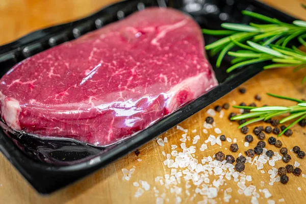 Beef steak in vacuum skin packaging and spices on wooden chopping board — Stock Photo, Image