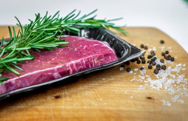 Vakumlu deri ambalajında biftek ve kopyalanmış ahşap kesme tahtasındaki baharatlar.