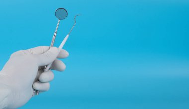 Diş hekimi hastanın diş muayenesini göstermek için monte edilmiş bir ayna tutuyor..