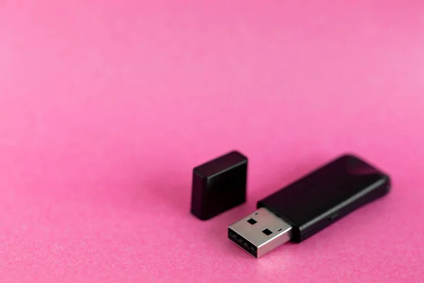 Black USB removable storage device on pink colorful background with copy space for text