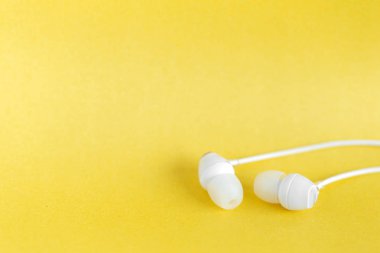 Sarı pastel arka planda beyaz kulaklıklar ve metin için kopyalama alanı