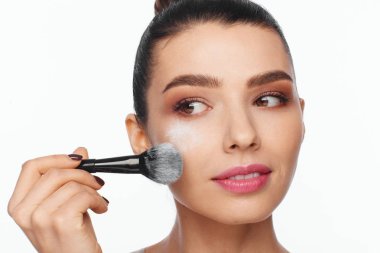 Bir fırça onun elinde tutan ve yüzünü bir fırça ile toz uygulamak güzel bir genç kadının portresi. Beyaz arka plan