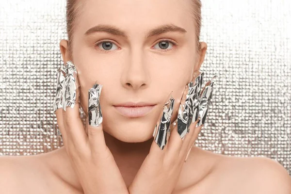 Portrait of a young beautiful woman on a futuristic background, with fingers wrapped in foil