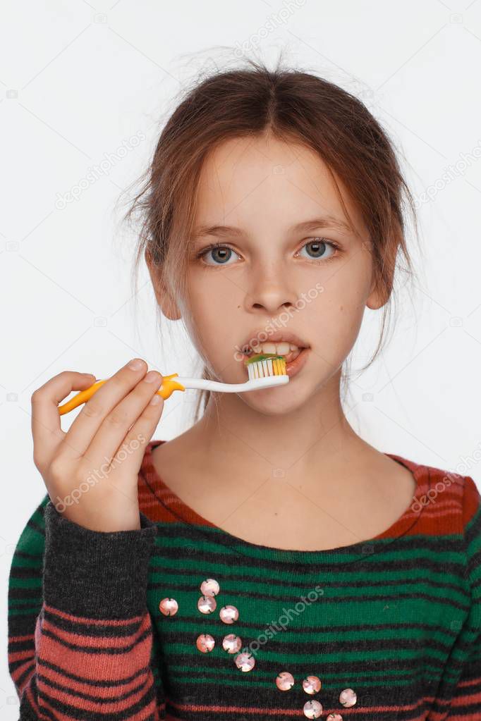 Portrait of an eight-year-old girl who brushes her teeth with a toothbrush. Striped sweater