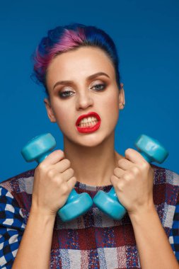 Onu mavi dumbbells ile mavi ve pembe saçlı bir kadın portresi Studio eller ve kareli bir bluz giymiş