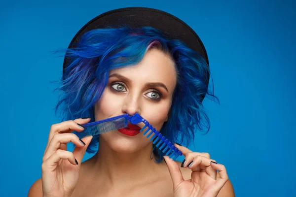 Retrato de uma mulher com cabelo azul em um chapéu preto e com uma escova de cabelo azul na mão — Fotografia de Stock