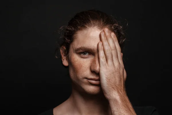 Portrait of a handsome long-haired man with drawn hair and freckles wearing a black T-shirt