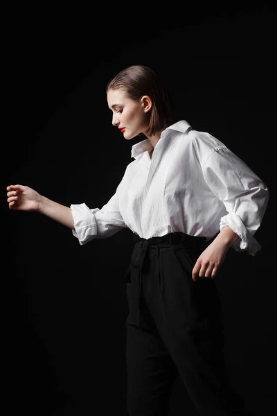 Портрет элегантной молодой женщины в белой рубашке и черных брюках. Интересный студийный свет — стоковое фото