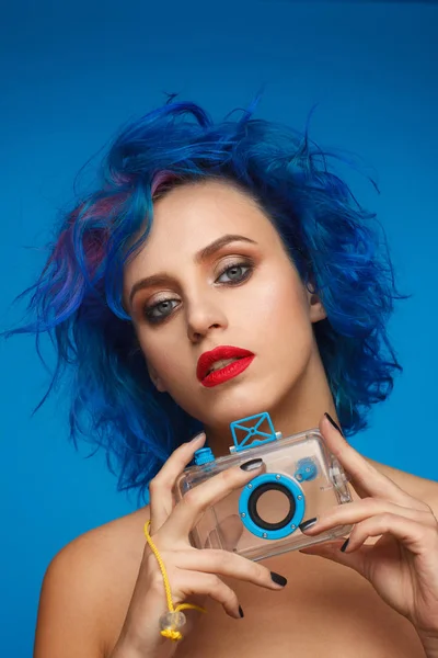 Retrato de una mujer extravagante con cabello azul y rosa y labios rojos sosteniendo una maqueta de cámara de plástico — Foto de Stock