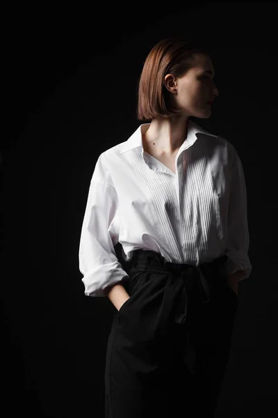 Retrato de una joven elegante con camisa blanca y pantalones negros. Interesante luz de estudio — Foto de Stock