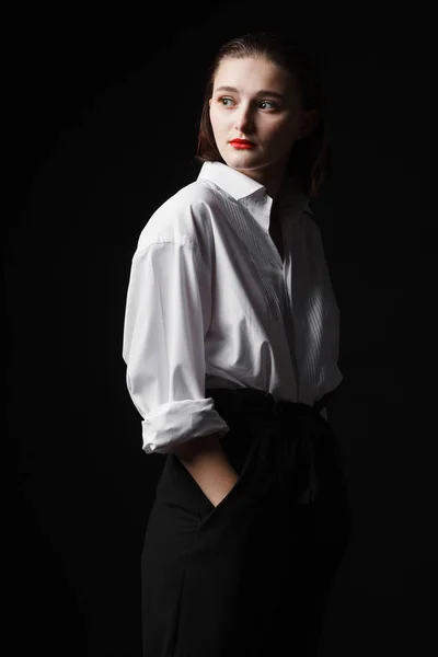 一个优雅的年轻女子的肖像, 穿着白衬衫和黑色裤子。有趣的工作室灯 — 图库照片