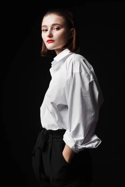 Ritratto di una giovane donna elegante con camicia bianca e pantaloni neri. Interessante luce da studio — Foto Stock