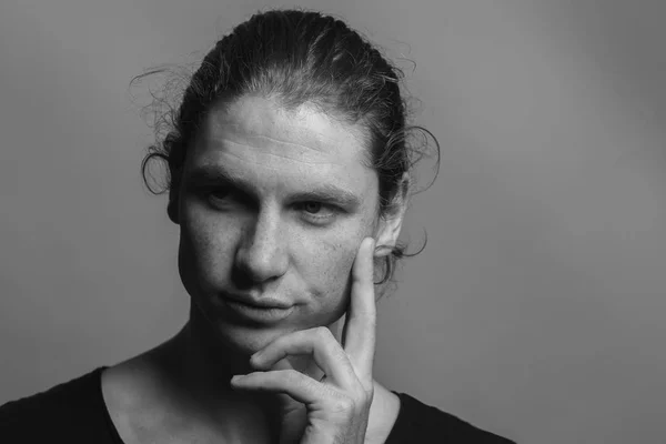 Portrait of a handsome long-haired man with drawn hair and freckles wearing a black T-shirt