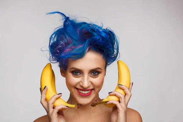 バナナを手に持った青とピンクの髪と笑う女性のポートレートには、携帯電話が好きです。スタジオ フォト セッション — ストック写真