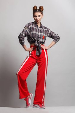 Eğlenceli, olumlu model bir ekose gömlek, kırmızı eşofman ve spor ayakkabı giyen bir resim. Studio fotoğraf oturum