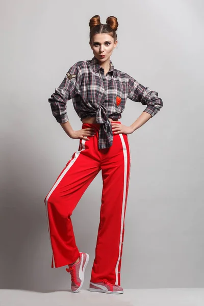 Eğlenceli, olumlu model bir ekose gömlek, kırmızı eşofman ve spor ayakkabı giyen bir resim. Studio fotoğraf oturum