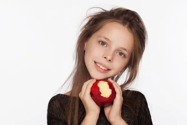 Красивая эмоциональная восьмилетняя девочка с яблоком. Фотосессия в студии. На девушке чёрная блузка. — стоковое фото