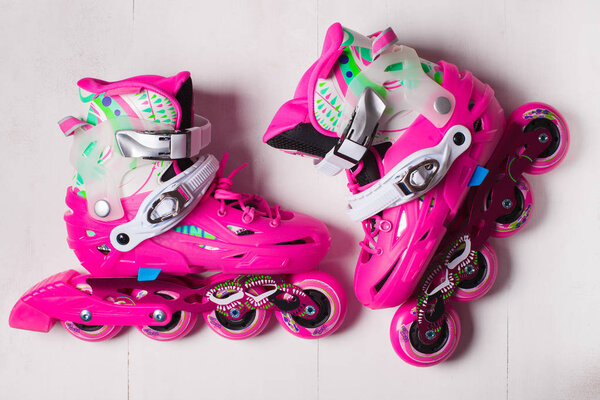 A pair of pink stylish roller skates on a white wooden background