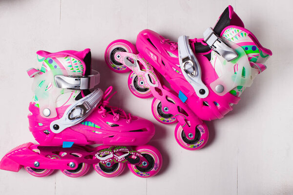 A pair of pink stylish roller skates on a white wooden background