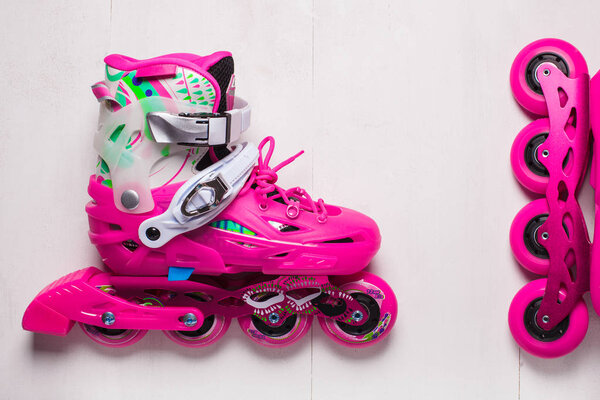 A pair of pink stylish roller skates on a white wooden background