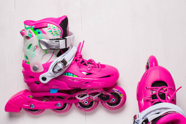 A pair of pink stylish roller skates on a white wooden background