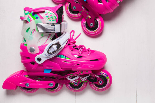 A pair of pink stylish roller skates on a white wooden background